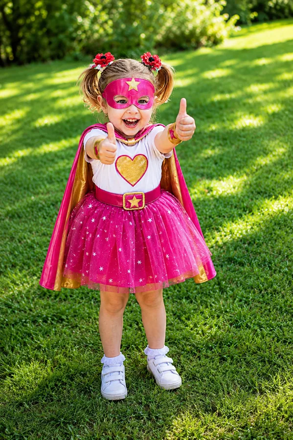 Young child in a superhero costume giving two thumbs up while playing outdoors